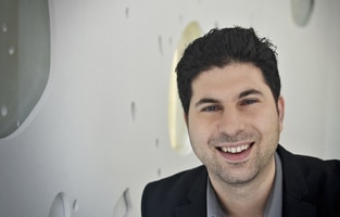 A man smiling in front of a white wall is featured in a Podcast Episode.