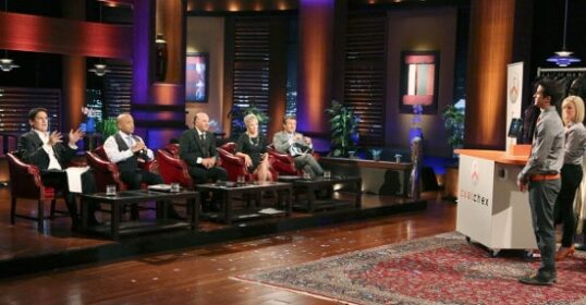 A group of people sitting in chairs on a Shark Tank stage.