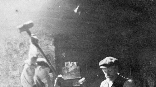 Two men providing manhood in a blacksmith shop.