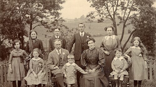 An old photo of a family posing in front of a fence, capturing the essence of familial bonds and heritage.
