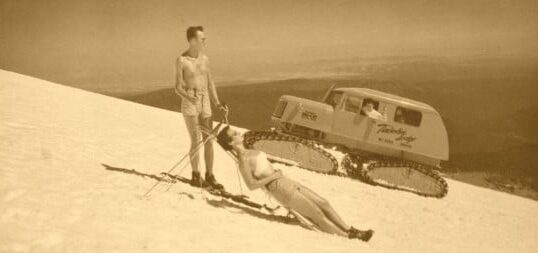 A man and woman enjoying spring skiing on a snowy slope, with a truck parked behind them.