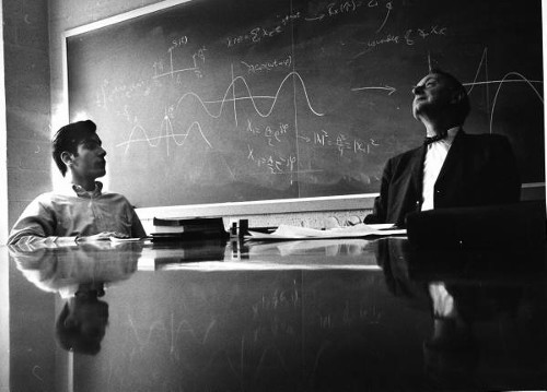 Vintage college student with his professor in a classroom sitting in front of board..