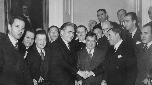 A group of men are meeting and shaking hands to strengthen their introductions at a table.