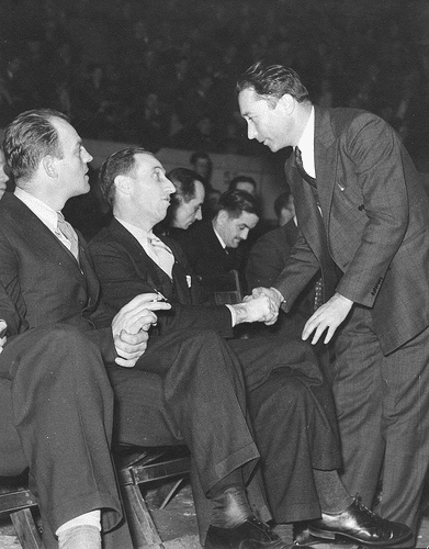 Vintage businessman shaking hands with man sitting in arena.