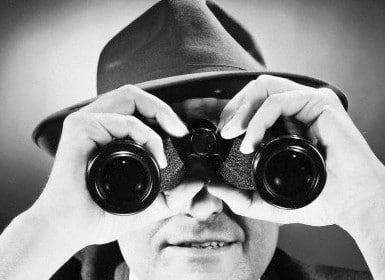 A man wearing a hat, going undercover and discreetly protecting his privacy online, intently looks through binoculars.