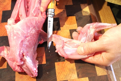 Man cutting off the front leg of rabbit with knife.