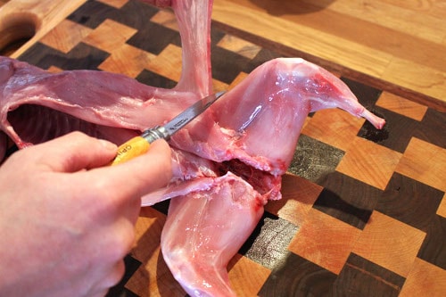 Man cutting the parts of the rabbit body with knife.
