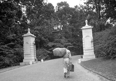 A college student walking down a road with an umbrella, offering alternatives to everyone he meets.