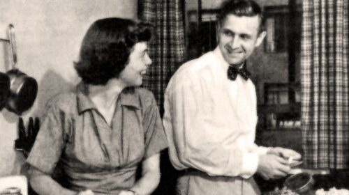 An old black and white photo of a man and woman preparing dinner in a kitchen.