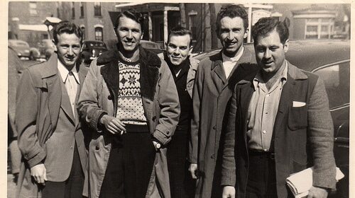 A conflicted group of men standing in front of a modern age car, questioning their manhood.