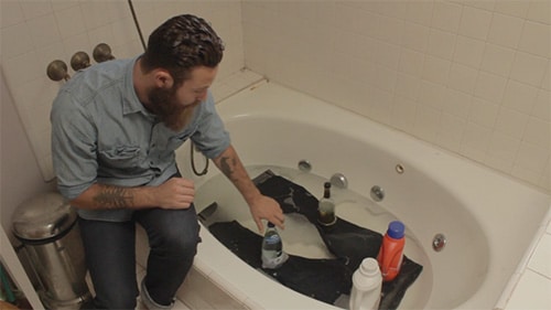 Man washing denim jeans in bathtub. 