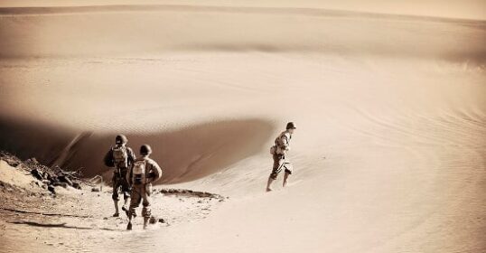 Two people showcasing their masculinity as they walk down a sand dune, captured in a sepia tone.