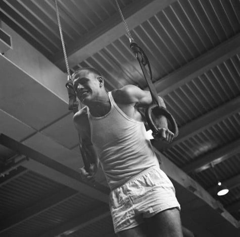 Vintage gymnast hanging on gymnastic rings. 