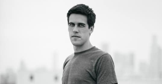 A black and white photo of a man standing in front of a city featured on the Art of Manliness website.
