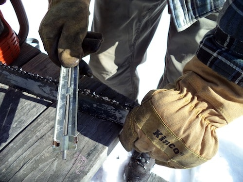 A man using file guide to sharpen the chainsaw.