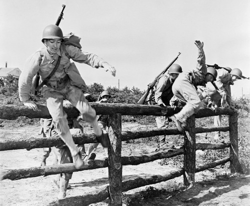 Vintage soldiers jumping over wooden fence at bootcamp.