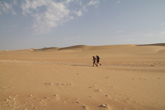 Desert ultra marathon two men running side by side on sand.