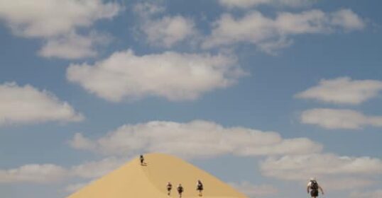 A group of people overcoming obstacles while hiking up a sand dune.