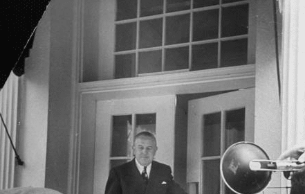 A man in a suit enters the room and is being photographed by a cameraman.