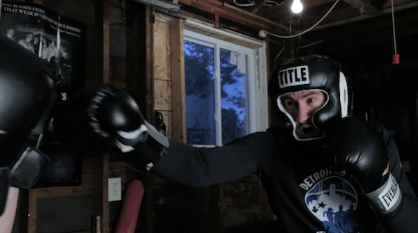 Man in garage boxing gear punching speed bag.