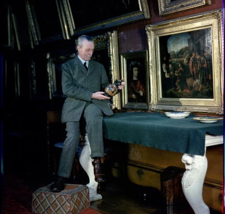 A man in a suit sitting at a table in front of paintings, appearing to invest.