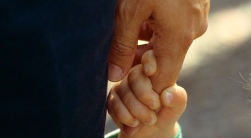 A close up of a dad holding a child's hand.
