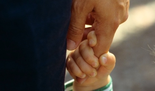 A close up of a dad holding a child's hand.