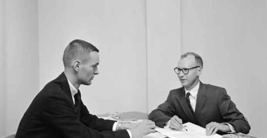 Two men in suits sitting at a desk.