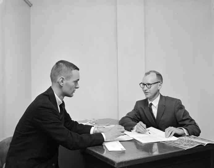 Two men in suits sitting at a desk.