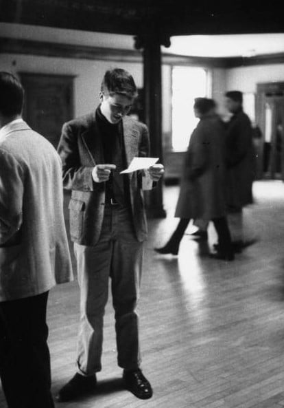 Vintage young man reading letter in open lobby.