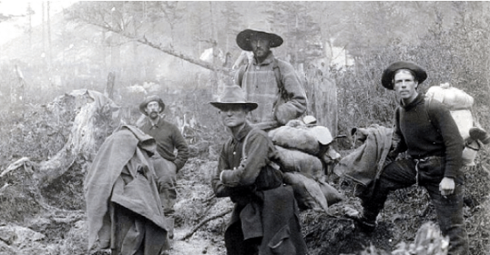 A group of men standing in the wooded area, dressed in outdoor gear.