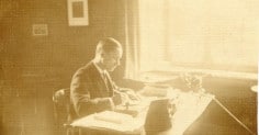 An old photo of a man writing at a desk.