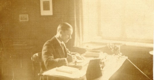 An old photo of a man writing at a desk.