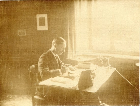 An old photo of a man writing at a desk.