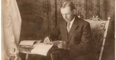 An old photo of a man writing in a chair.