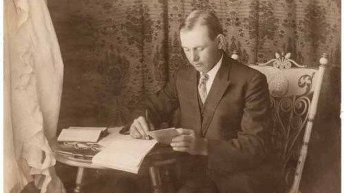 An old photo of a man writing in a chair.
