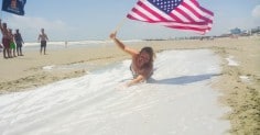 A man laying in the sand with an American flag.