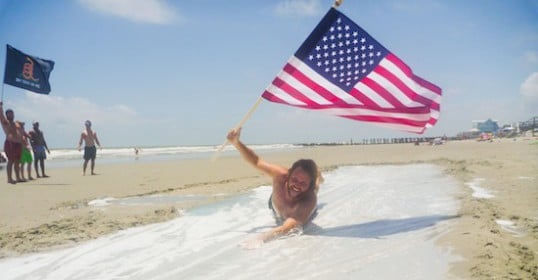 A man laying in the sand with an American flag.