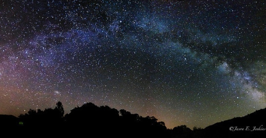 The man can find constellations in the milky night sky above a mountain.