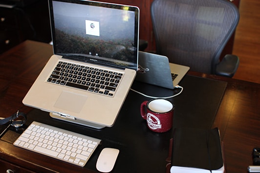 A cup is placed at Table with laptop and Mouse.