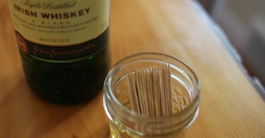 A bottle of whiskey next to a jar of toothpicks for DIY cocktail garnishes.