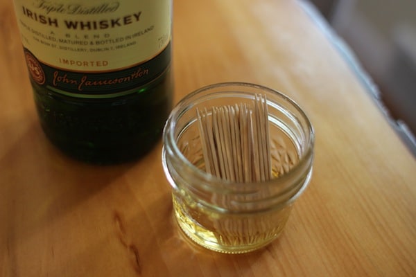 A bottle of whiskey next to a jar of toothpicks for DIY cocktail garnishes.