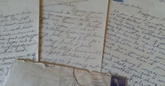 A collection of old letters and postcards on a table, possibly written by a WWII Grandpa.