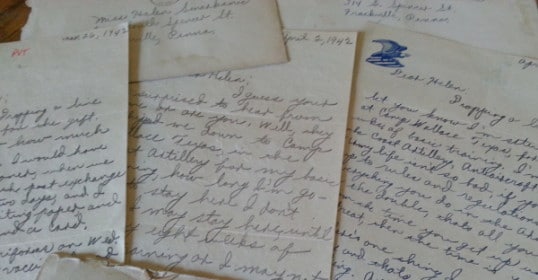 A collection of old letters and postcards on a table, possibly written by a WWII Grandpa.