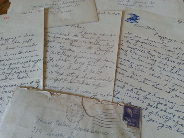 A collection of old letters and postcards on a table, possibly written by a WWII Grandpa.