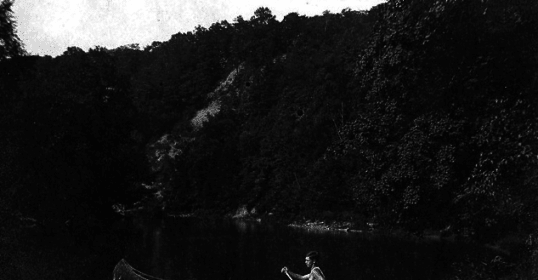 A man embarks on a canoe journey across a serene lake, marking a personal rite of passage.