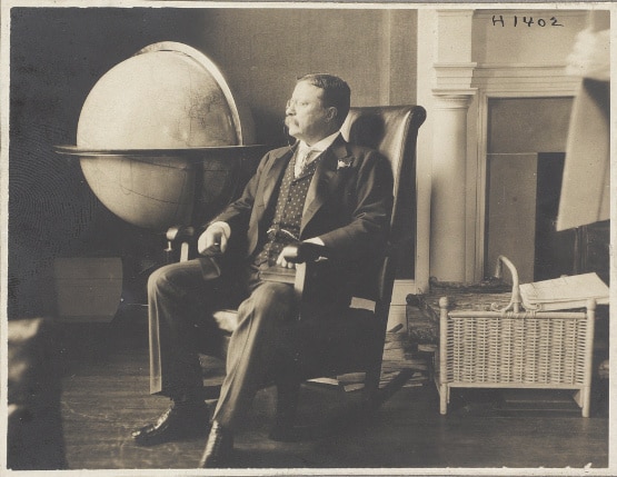 Teddy Theodore sitting on chair with giant globe.