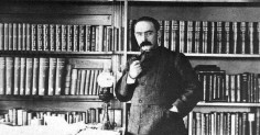 A man in a suit standing in front of a bookshelf from the Gentleman's Guide to Collecting Books.