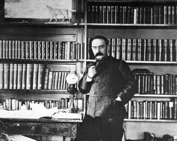 Rudyard Kipling smoking a pipe in library. 