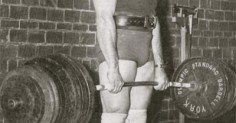 A man holding a barbell in front of a brick wall looks stronger.